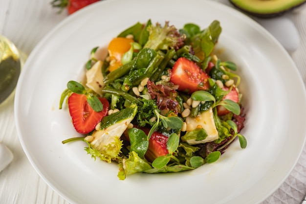 Salat mit Erdbeeren Brie-Käse-Tomaten und Gemüse auf einem weißen Teller und einem weißen Tisch