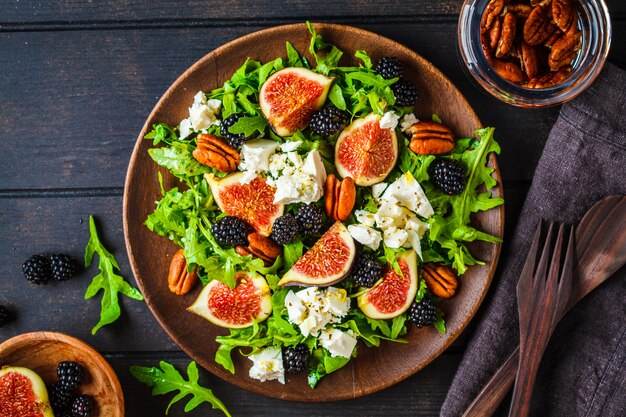 Salat mit Feigen, Feta und Brombeeren in einer Holzplatte auf dunklem Hintergrund, Ansicht von oben,