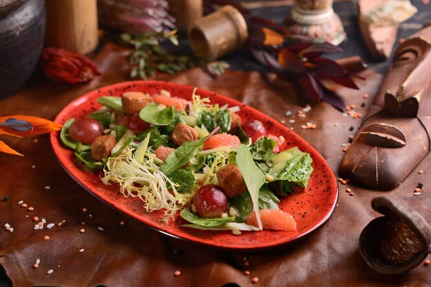 Salat mit Fleisch, Trauben und Orange. In einer roten Platte. Afrikanisches Dekor