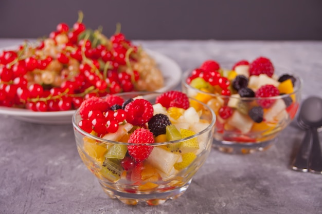 Salat mit frischen Früchten und Beeren auf Schalen auf dem konkreten Hintergrund