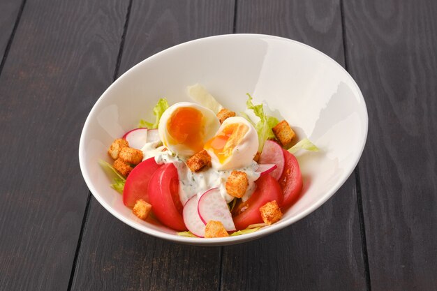 Salat mit frischen Tomaten in der Nähe von Radieschen und gekochtem Ei