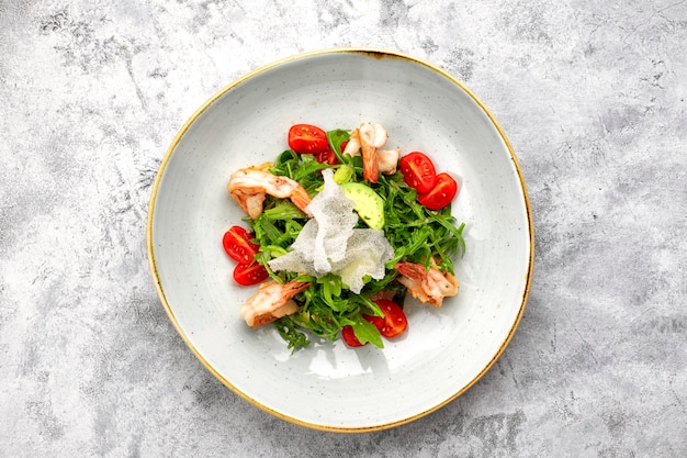 Salat mit Garnelen, Tomaten und Rucola, auf einem weißen Teller, auf hellem Hintergrund
