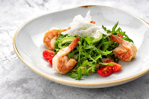 Salat mit Garnelen, Tomaten und Rucola, auf einem weißen Teller, auf hellem Hintergrund