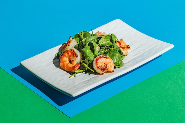 Salat mit Garnelen und Rucola auf weißem Teller auf farbigem Hintergrund