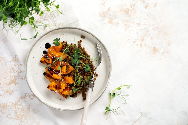 Salat mit gebackenem Kürbis, Linsen und Balsamico-Dressing garniert mit Erbsen-Microgreens auf hellem Hintergrund. Gesundes veganes Essen, Draufsicht