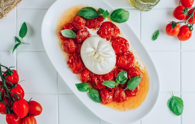 Salat mit gebackenen Tomaten und Burrata auf weißem Fliesenhintergrund Italienische Küche Gesunde Ernährung Vegetarische Küche