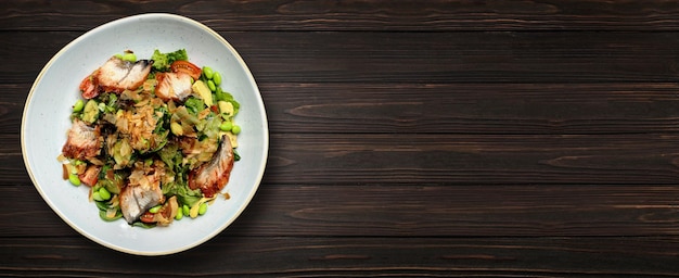 Salat mit gegrilltem Aal und Gemüse auf einem Teller auf Holzhintergrund