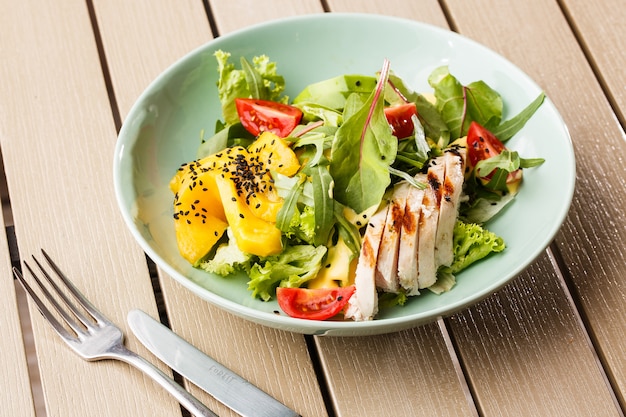 Salat mit gegrilltem Hähnchen, Mango, Salat, Avocado, Tomaten, Rucola, Käsesause auf einem weißen Teller