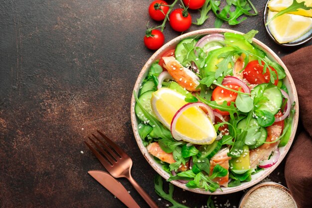 Salat mit gegrillten Hühnertomaten, Rucola, roten Zwiebeln, Avocado, Sesamsamen und Zitronenöl-Dressing Gesundes Essen Draufsicht