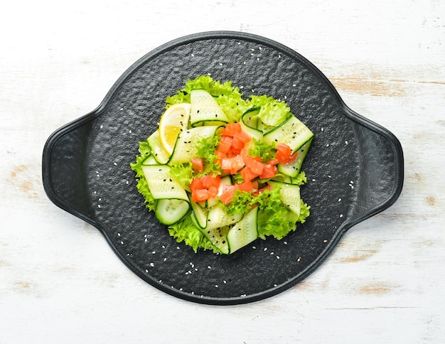 Salat mit Gurke, Lachs und Kopfsalat. Gesundes Essen. Auf einer schwarzen Steinplatte. Ansicht von oben.