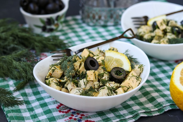 Salat mit Huhn, Käse und schwarzen Oliven in den weißen Schüsseln auf dem Tisch