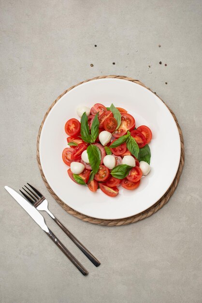 Salat mit Kirschtomaten und Mozzarella auf einem weißen Teller auf grauem Hintergrund