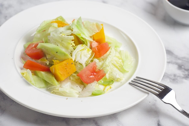 Salat mit Kohl-Tomaten-Gurken-Kürbis in einem Teller auf dem Marmortisch