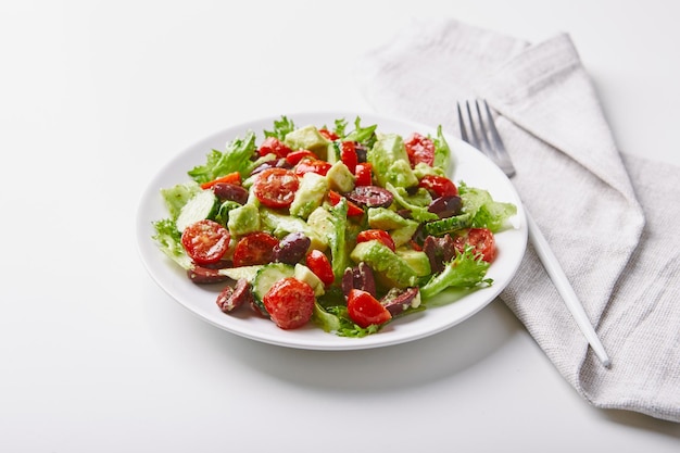 Salat mit Kopfsalat, Gurken, Tomaten, Oliven und Avocados in weißer Platte auf dem Tisch