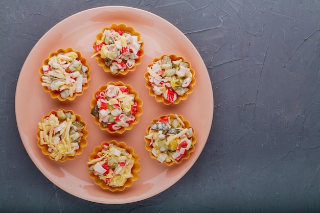 Salat mit Krabben in Törtchen auf einem beigen Teller auf schwarzem Hintergrund kopieren. Horizontales Foto