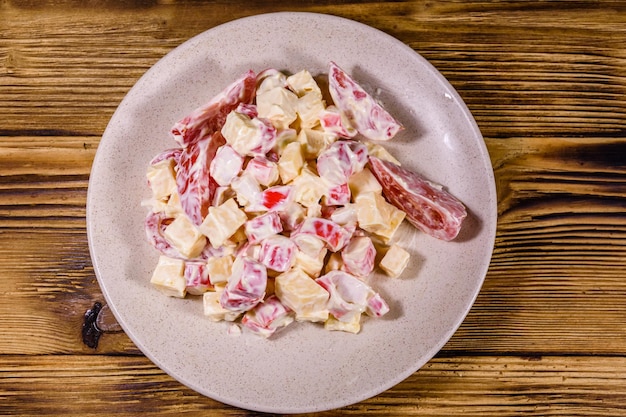 Salat mit Krabbenstäbchen, Käse und Tomaten mit Mayonnaise auf einem Holztisch. Ansicht von oben