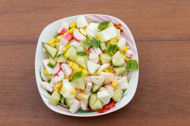 Salat mit Krabbenstäbchen, Mais, Gurke und Eiern auf Holztisch. Ansicht von oben