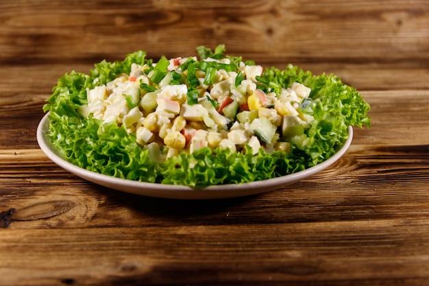 Salat mit Krabbenstäbchen, Mais, Gurken, Eiern, Reis und Mayonnaise auf Holztisch