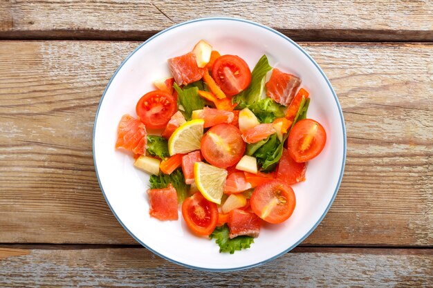 Salat mit Lachs und Kirschtomaten und grünem Salat in einem Teller auf einem Holztisch