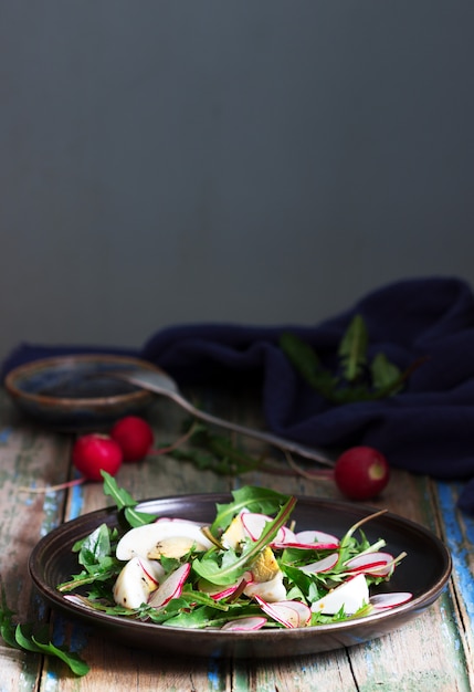 Salat mit Löwenzahn, Ei und Rettich auf einem hölzernen Hintergrund. Rustikaler Stil.