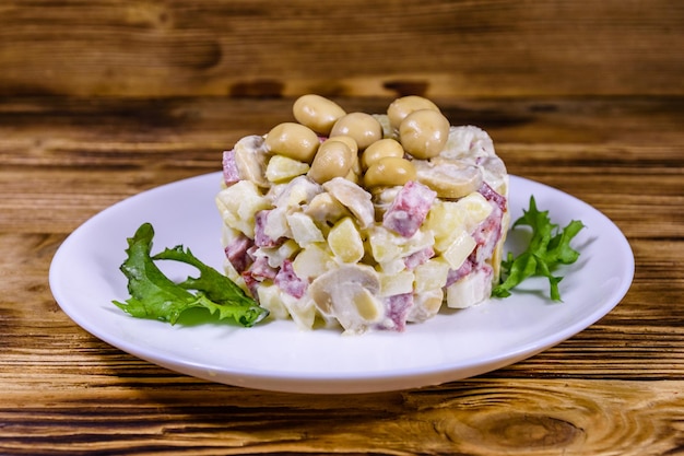 Salat mit marinierten Champignons, Wurst, Zwiebeln, Salzkartoffeln und Mayonnaise auf einem Holztisch