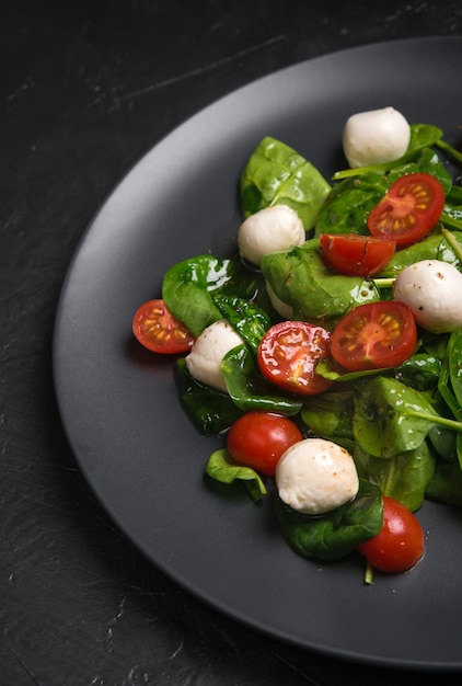 Salat mit Mozzarella und Babyspinat auf schwarzer Keramikplatte.