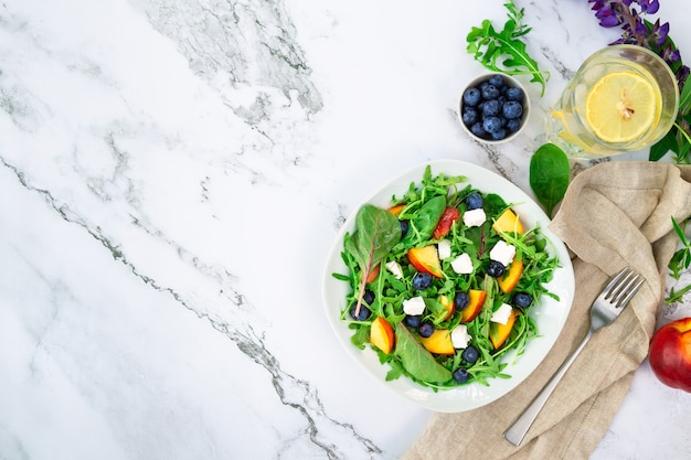 Salat mit Nektarinen Blaubeeren Rucola-Spinat und Feta-Käse auf weißem Marmorhintergrund