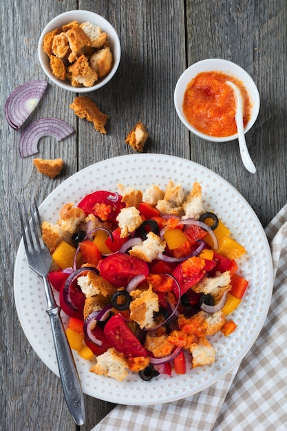 Salat mit Paprika, Tomaten, Zwiebeln, Oliven und Croutons mit Sousomna alter Holzoberfläche