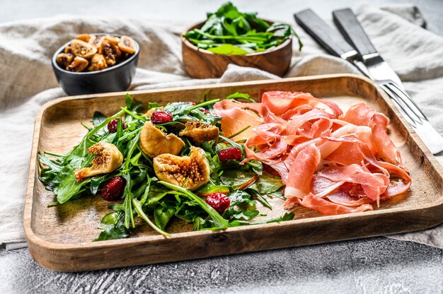 Salat mit Parma, Schinken, Rucola und Feigen. Italienische Antipasti. Grauer Hintergrund, Draufsicht.