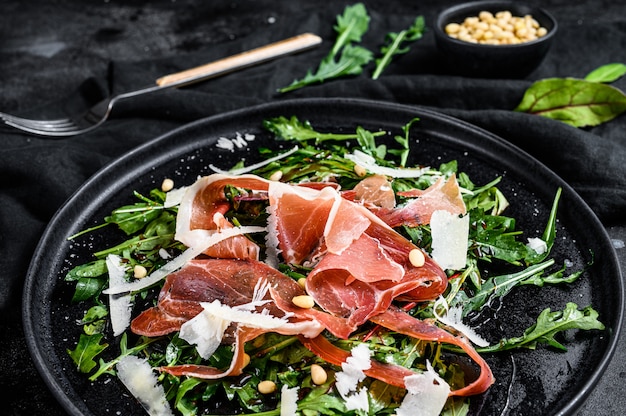 Salat mit Parma, Schinken, Rucola und Parmesan. Schwarze Oberfläche, Draufsicht.