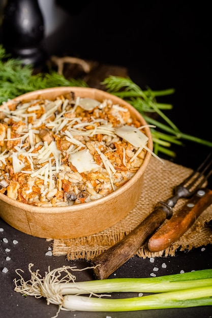 Salat mit Pilzen und Käse in einem Papierbehälter, Schneidebrett mit Sackleinen, Kräutern und Soße,