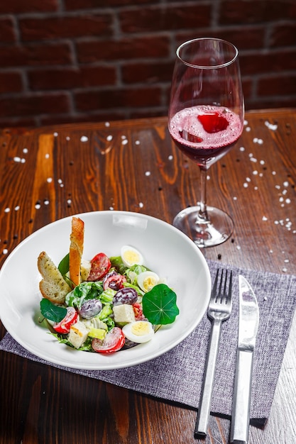 Salat mit Prosciutto, Traubenschnitten und Kirschtomaten, Wachteleier auf einem Teller und ein Glas Wein