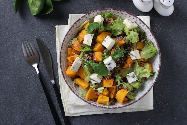 Salat mit Quinoa, Kürbis und Dor Blauschimmelkäse in einem Teller auf einer dunklen Oberfläche. Sicht von oben