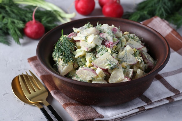 Salat mit Radieschen, Frühlingszwiebeln, Eiern und Dill, gewürzt mit Sauerrahm in einer dunklen Schüssel auf einem Grau