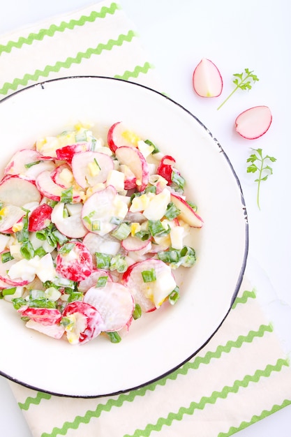 Foto salat mit rettich, frühlingszwiebel und ei in einer weißen platte. weißer hintergrund.