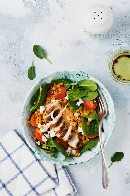 Salat mit roten Linsen, Spinatblättern, Kirschtomaten, Hühnerfleisch und Mozzarella-Käse mit Olivenöl in Keramikplatte auf altem grauem Betonhintergrund