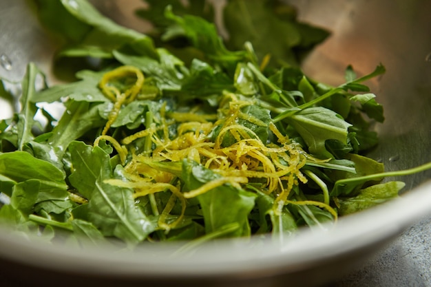 Salat mit Rucola und Orangenschale in Metallschüssel.