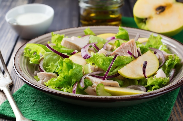 Salat mit Salat, Apfel, Sellerie, Zwiebel und Huhn auf dem grauen Teller auf dunkler Holzoberfläche