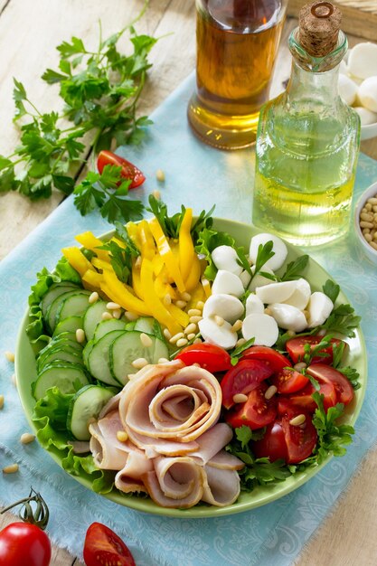 Salat mit Schinken, frischem Gemüse, Pinienkernen und Mozzarella auf dem Küchenholztisch