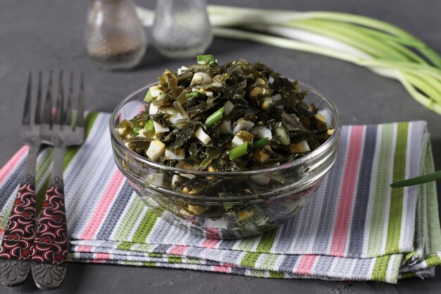 Salat mit Seetang, Ei und Frühlingszwiebeln in einer transparenten Schüssel auf grauem Hintergrund. Nahaufnahme