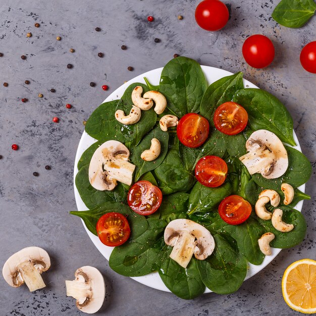 Salat mit Spinat, Pilzen und Tomaten auf Beton.