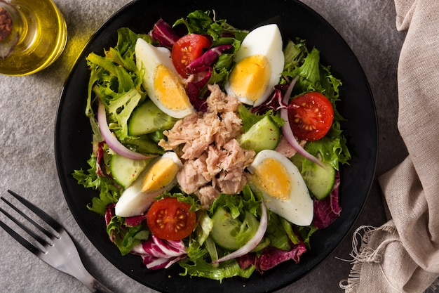 Salat mit Thunfisch, Ei und Gemüse auf Schwarzblech und grauem Hintergrund