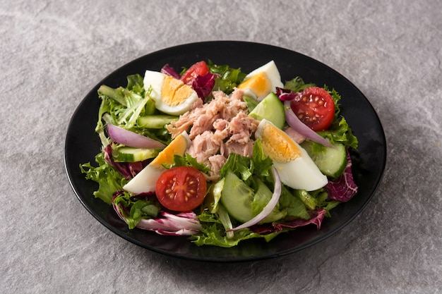 Salat mit Thunfisch, Ei und Gemüse auf Schwarzblech und grauer Oberfläche