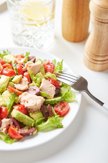 Salat mit Thunfischsalat, Gurken, Tomaten, Oliven und Avocados in weißer Platte auf dem Tisch