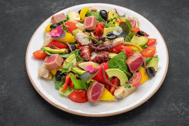 Salat mit Tintenfisch, Thunfisch und Gemüse auf dunklem Hintergrund