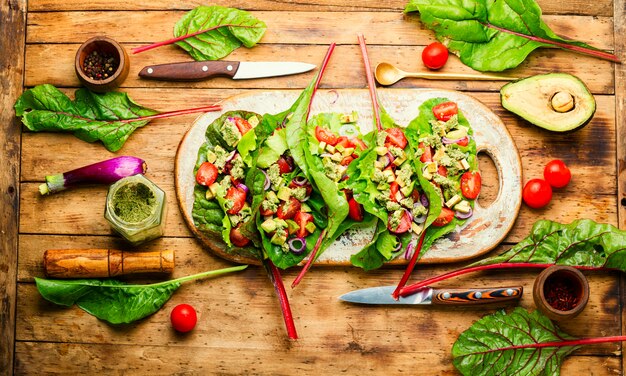 Salat mit Tomaten,Avocado,Knoblauchsauce in Mangoldblättern.Sommerlicher Vitaminsalat auf Küchenbrett