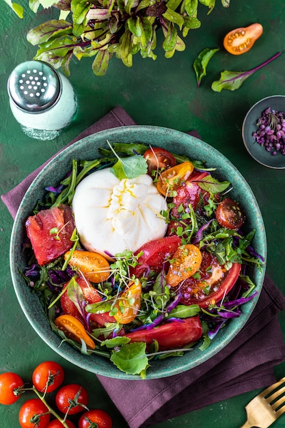 Salat mit Tomaten, Rucola, Burrata-Käse und Microgreens auf grünem Steinhintergrund, Draufsicht, vertikal