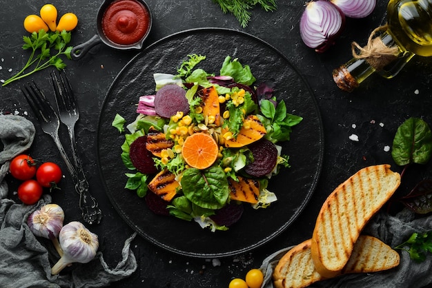 Salat Rote-Bete-Kürbis Mais und Kopfsalat in einer schwarzen Platte auf schwarzem Hintergrund Draufsicht Freier Platz für Ihren Text