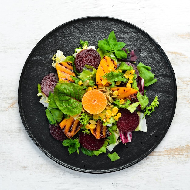 Salat-Rote-Bete-Kürbis-Mais und Kopfsalat in einer schwarzen Platte auf weißem Holzhintergrund Draufsicht Freier Platz für Ihren Text
