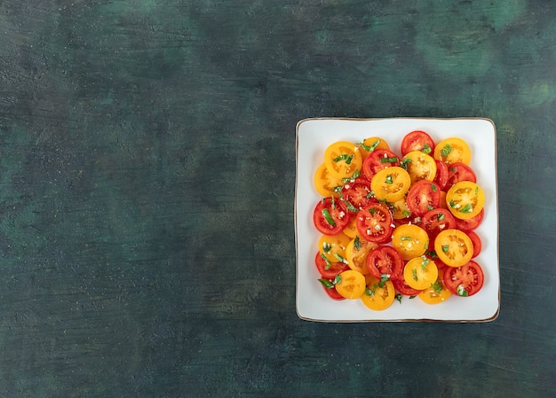 Salat von frischen roten und gelben Tomaten mit Basilikum auf einem dunklen Hintergrund